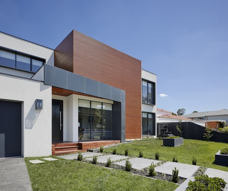 Maison contemporaine à l'architecture moderne, façade bois et blanc, jardin paysager avec chemin de dalles carrées.